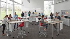 people are working at desks in an open room with lots of windows and large windows