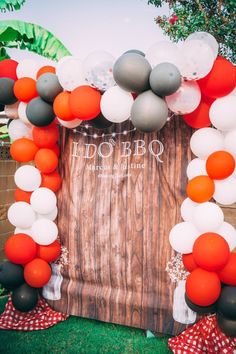 an orange and white balloon arch is set up in front of a wooden backdrop with balloons