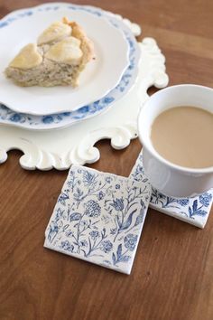 a cup of coffee sitting on top of a wooden table next to a plate with food