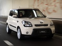 a white car driving down a street next to a wall