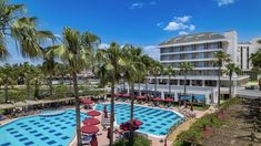 an outdoor swimming pool surrounded by palm trees and lounge chairs with red umbrellas in the sun