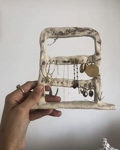 a hand holding up a small white frame with jewelry hanging from it's sides