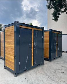 three portable toilets are lined up outside on the concrete and one is closed with wood paneling