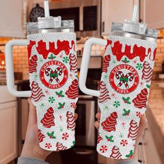 two christmas themed tumblers are being held up in the kitchen