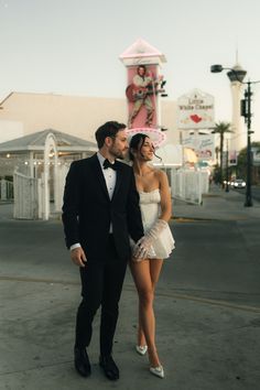 a man in a tuxedo standing next to a woman wearing a short white dress