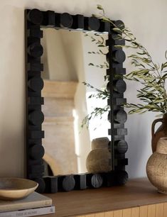 a mirror sitting on top of a wooden table next to a vase and potted plant