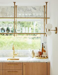 a kitchen with marble counter tops and wooden cabinets, gold faucets, wine glasses on the window sill