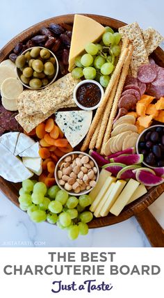 a wooden platter filled with cheese, crackers, olives, and grapes