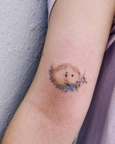 a small hedgehog tattoo on the left inner arm and shoulder with blue flowers around it