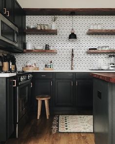 a kitchen with black cabinets and white tile backsplash, wood flooring and open shelving