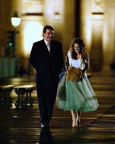 a man and woman are walking down the street at night, dressed in formal attire