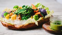 a wooden bowl filled with lots of different types of vegetables next to a jar of pestle