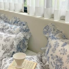 a coffee cup and book on a bed with blue floral bedspreads in front of the window