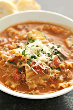 a white bowl filled with pasta and meat soup on top of a black table next to slices of bread