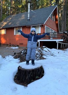 a young boy standing on top of a tree stump in front of a red house