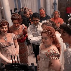 a group of people standing around each other in formal dress and tiaras, with one woman wearing a crown on her head