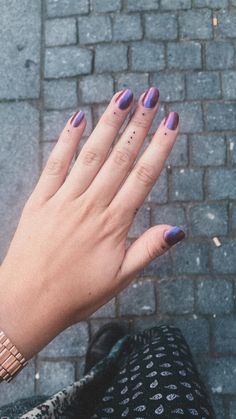 a woman's hand with purple and black nail polish on it, holding her left hand out in front of the camera