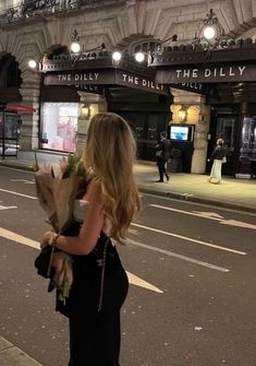 a woman walking down the street with flowers in her hand