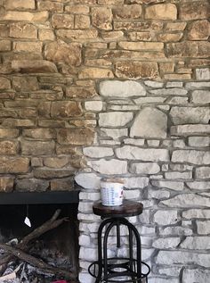 a fire place with a brick fireplace and stone wall in the background, next to an old fashioned bar stool