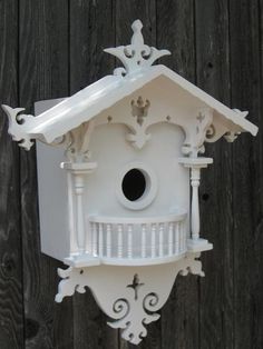 a white birdhouse with an ornate design on the top and bottom part, attached to a wooden fence