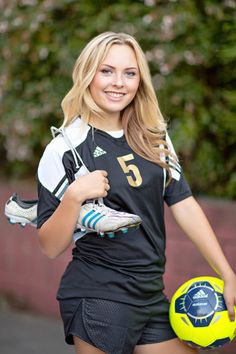 a young woman holding a soccer ball in her right hand and posing for the camera