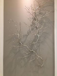 a white tree branch is hanging on the wall in front of a gray background with light coming from behind it