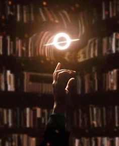 a person holding up a small object in front of a bookshelf at night