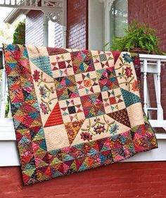 a colorful quilt hanging on the side of a brick building next to a white porch