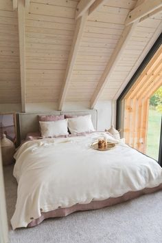 a bed with white sheets and pillows in a bedroom next to an open window that looks out onto a grassy field