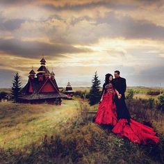 a man and woman are standing in the middle of a field with an old church behind them