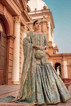 a woman in a blue and green lehenga standing on the steps with her hands behind her back