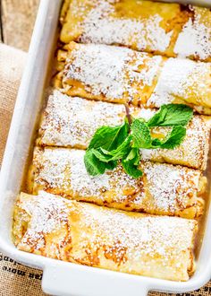 some food that is in a white dish on a table with green leaves and powdered sugar