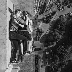 black and white photograph of two people kissing on a ledge