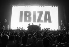 a large group of people at a concert with their hands up in front of an ibiza sign