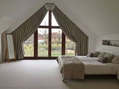 a large bed sitting in a bedroom next to a tall window with curtains on it