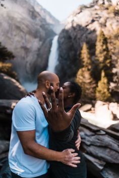 two people standing next to each other with their hands in the air near a waterfall