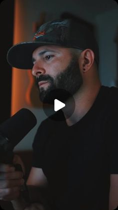 a man with a beard wearing a baseball cap and holding a microphone in front of him