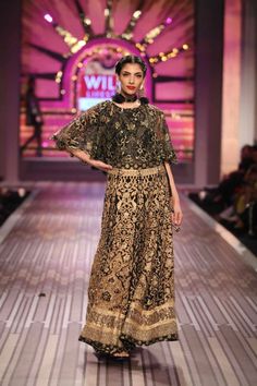 a model walks down the runway in a black and gold gown with an elaborate neckline