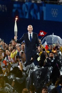 a man in a suit and tie holding an olympic torch while surrounded by people with umbrellas