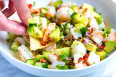 a person is picking up some food from a bowl with shrimp and avocado