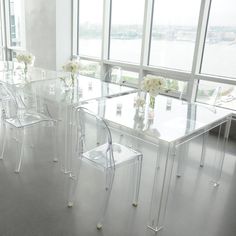 a dining room table with clear acrylic chairs and flowers in vases on it