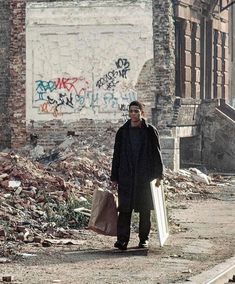 a man is walking down the street with his suitcases in hand and graffiti on the wall behind him