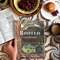 a person is reading a book on a table with grapes, muffins and coffee