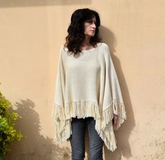 a woman standing against a wall with her hands in her pockets, wearing a sweater and jeans