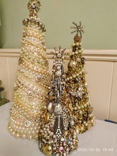 three small christmas trees are sitting on a table with pearls and other ornaments around them