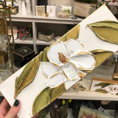 a person holding up a piece of paper with flowers on it in front of a shelf