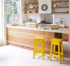 two yellow stools sit in front of a kitchen island with open shelving on the wall