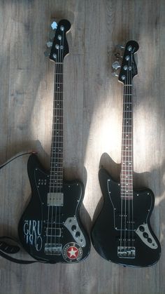 two black guitars sitting on top of a wooden floor next to each other, one with an electric guitar in it