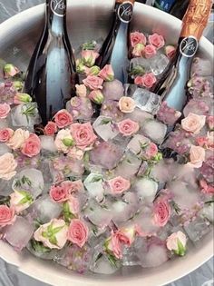 four bottles of champagne and ice in a bowl with pink flowers on the rims