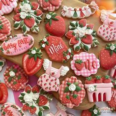 some very pretty decorated cookies on top of a cutting board with strawberries and strawberrys